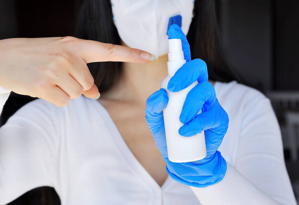 Концепция защиты от бактерий и вирусов. Женщина в хирургической маске и перчатках, защищает от гриппозной болезни, держит в руках белый спрей с алкоголем для дезинфекции
 - Фото, изображение
