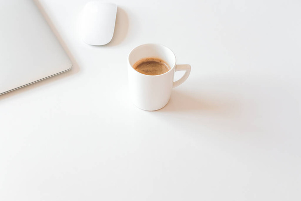 Чашка кофе и серебряный ноутбук на белом столе. Кофейный перерыв в концепции домашнего офиса
.  - Фото, изображение