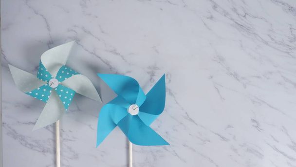 Wind wheel paper real toy on white color marble stone background which made from origami hand made on light blue colour japanese special material and wood stick for baby or kids playing. - Photo, Image