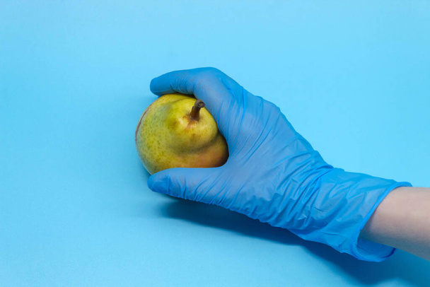 The man held out a blue-gloved hand. On the palm of your hand is a fresh pear - Photo, Image
