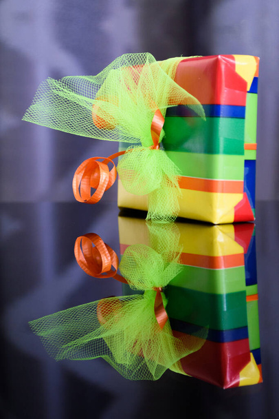 Vertical mirror image of a present: bright and colourful gift box isolated and reflected in the table below - Photo, Image