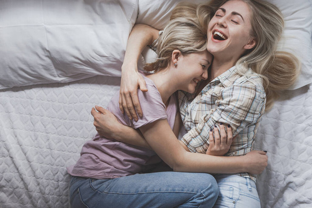 若い女の子のゲイレズビアンのカップルベッドの笑いと抱っこ、トップビューに横たわっている。愛とゲイの結婚と誇りの概念 - 写真・画像