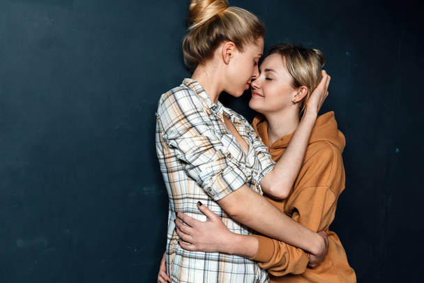 Loving lesbian girls hugging, standing on background of blue wall. Sequal opportunity Concept - Fotoğraf, Görsel