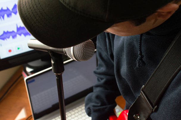 Young man with cap singing and playing electric guitar to record a song in his room. Music studio at home. - Photo, Image