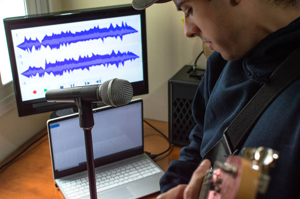 Jeune homme chantant et jouant de la guitare électrique pour enregistrer une chanson à l'aide du microphone et de la technologie. Musicien enregistrement de musique à la maison
. - Photo, image