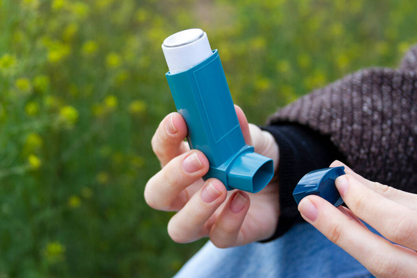 Ein Mädchen hält vor blühendem Hintergrund einen Asthma-Inhalator in der Hand. - Foto, Bild
