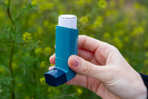 Ein Mädchen hält vor blühendem Hintergrund einen Asthma-Inhalator in der Hand. - Foto, Bild