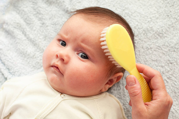 Bürsten Sie die Haare eines Babys von Hand mit einer weichen Bürste. Mutterschaftskonzept. Babyhygiene - Foto, Bild