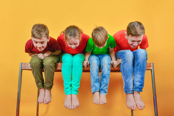As quatro crianças estão sentadas descalças, penduradas as pernas e inclinadas para baixo olhando para baixo
 - Foto, Imagem