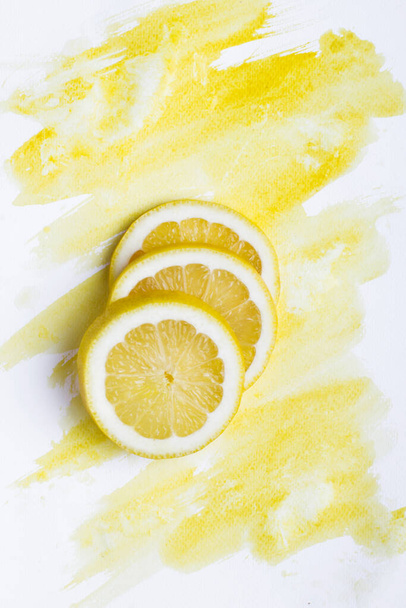 Top view of three lemon pieces on white paper with yellow watercolor - Photo, Image
