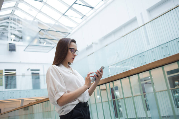 young positive business woman in glasses and a white shirt communicates in a messenger - Photo, image