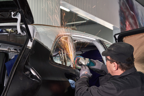 Reparaturarbeiter reparieren beschädigtes Auto. Arbeiten mit Winkelschleifer, um Metallkörper zu fixieren. - Foto, Bild