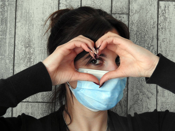 γυναίκα με μάσκα ζωγραφίζει μια καρδιά με τα χέρια της - Φωτογραφία, εικόνα