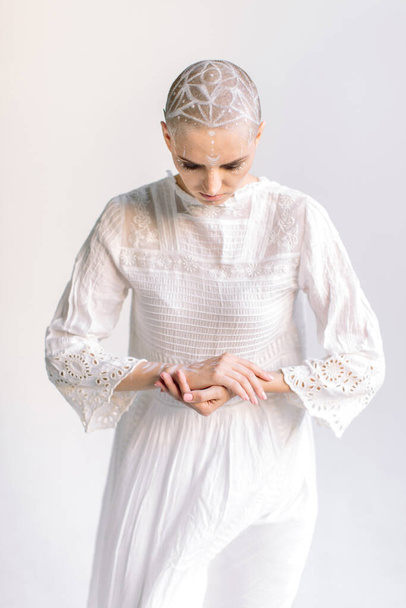 Calm woman gracefully holding hands and looking down in white dress with lace - Fotó, kép