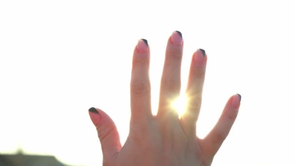 Una donna guarda il sole luminoso attraverso la mano. I raggi magici del sole brillano attraverso le dita. Fantastica luce brillante. Flash. Una donna che si crogiola al sole. Spensieratezza. Felicità. Turismo
. - Filmati, video