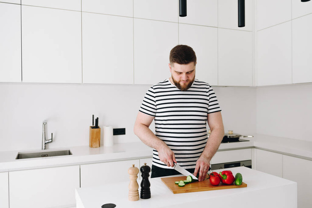 przystojny młody biały człowiek gotowanie a miło zdrowe warzywa posiłek lub sałatka w a nowoczesny jasny biały kuchnia - Zdjęcie, obraz