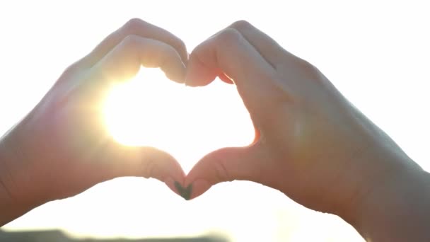 Woman makes hands in the shape of a heart in the bright sun. The magical rays of the sun shine through your fingers. Fantastic bright light. Symbol of love. Close up of attractive woman hands. - Footage, Video