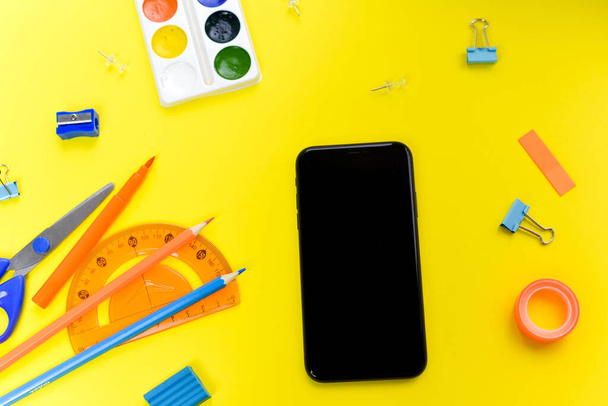 Office supplies near the phone on a yellow background. The concept of electronic distance learning. - Zdjęcie, obraz