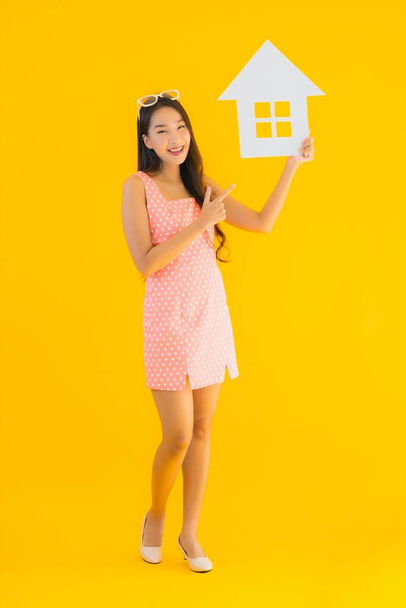 Portret mooie jonge aziatische vrouw tonen huis of huis teken op geel geïsoleerde achtergrond - Foto, afbeelding