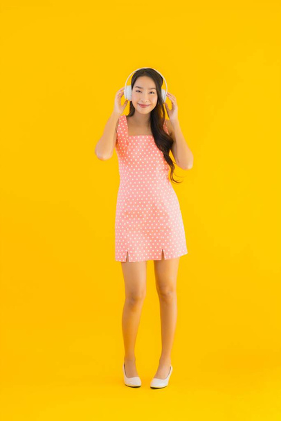 Ritratto bella giovane donna asiatica ascoltare musica con smart cellulare e cuffie su sfondo giallo isolato
 - Foto, immagini