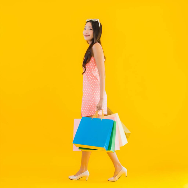 Πορτρέτο όμορφη νεαρή ασιατική γυναίκα με πολύχρωμο τσάντα ψώνια από πολυκατάστημα και εμπορικό κέντρο σε κίτρινο απομονωμένο φόντο - Φωτογραφία, εικόνα