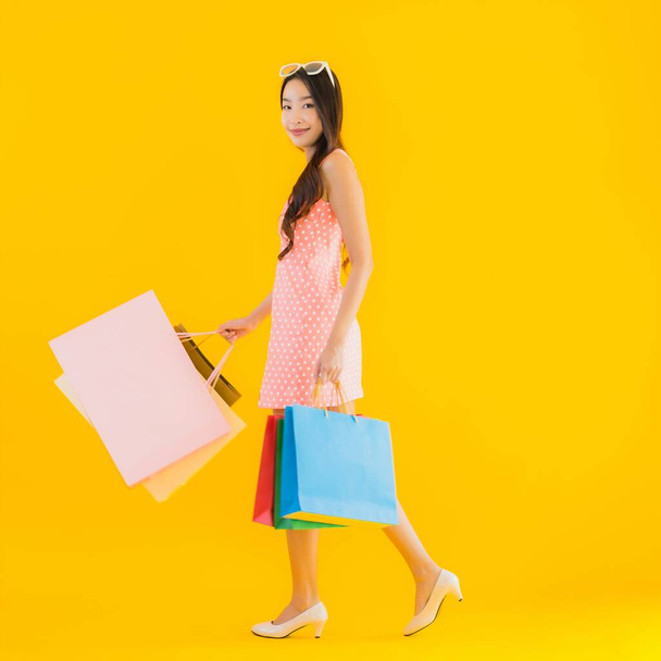 Retrato hermosa joven mujer asiática con colorido bolso de compras de grandes almacenes y centro comercial en amarillo aislado fondo
 - Foto, Imagen