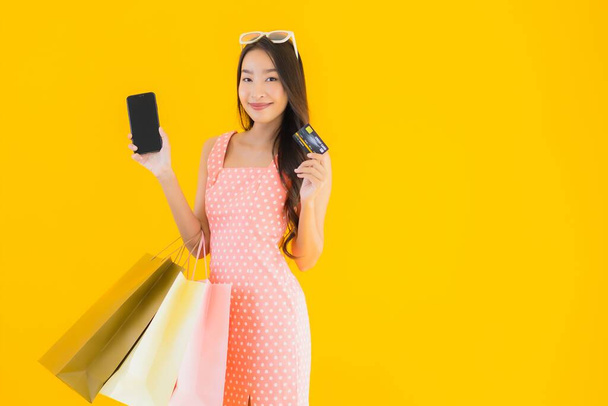 Muotokuva kaunis nuori aasialainen nainen värikäs ostoskassi älypuhelimella ja luottokortilla keltainen eristetty tausta
 - Valokuva, kuva