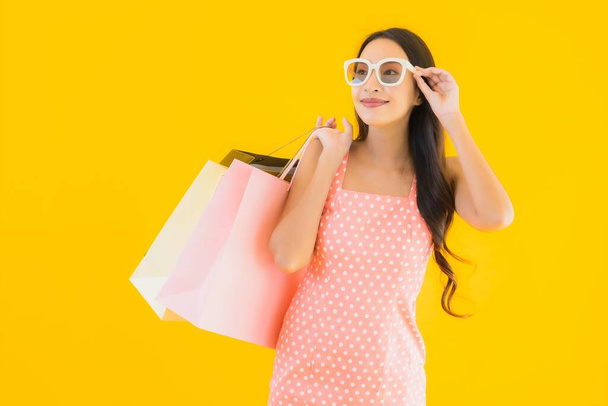 Retrato hermosa mujer asiática joven con colorido bolso de compras con teléfono móvil inteligente y tarjeta de crédito sobre fondo aislado amarillo
 - Foto, Imagen