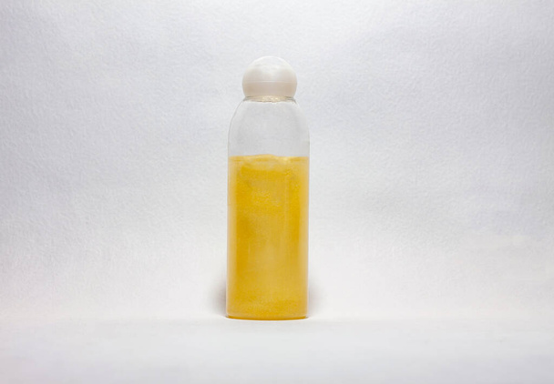 Одна стеклянная бутылка желтого геля для душа с белым колпачком на светлом фоне
.  - Фото, изображение
