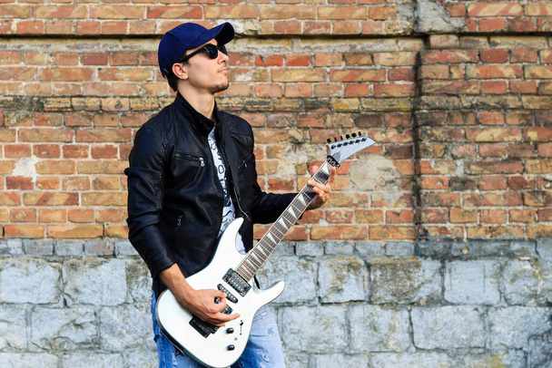 Молодой красивый парень в кожаной куртке играет на гитаре
 - Фото, изображение