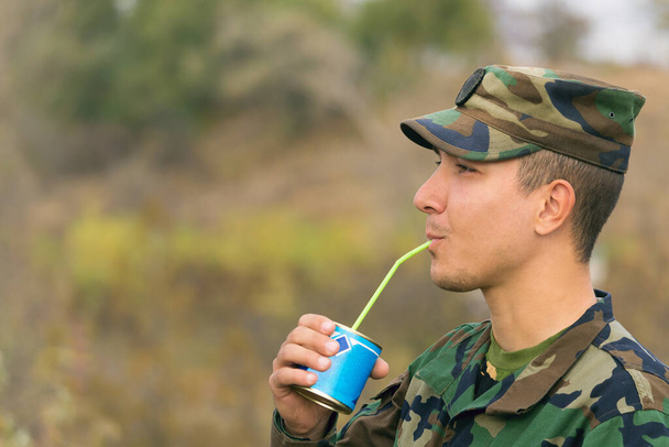 Zadowolony szczęśliwy głodny żołnierz pije skondensowane mleko przez słomkę, stonowane - Zdjęcie, obraz