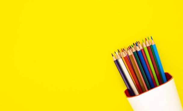 colored pencils in a white organizer, isolated on a yellow background. office supplies for preparing for school. background for designers with space for text - Photo, image