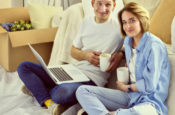 Couple buying online with a laptop and moving house sitting on the floor - Fotoğraf, Görsel