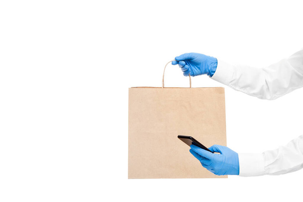 hands in sterile gloves of a courier for safe food delivery of an online order by cell phone during the quarantine pandemic of coronavirus covid-19 isolated on white with a copy space. - Photo, Image