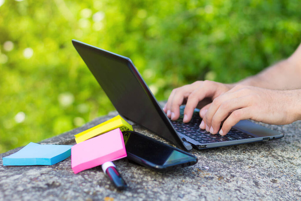 IT-specialist werkt buiten. Handen, laptoptoetsenbord, smartphone, marker en kleurstickers, afgezwakt - Foto, afbeelding