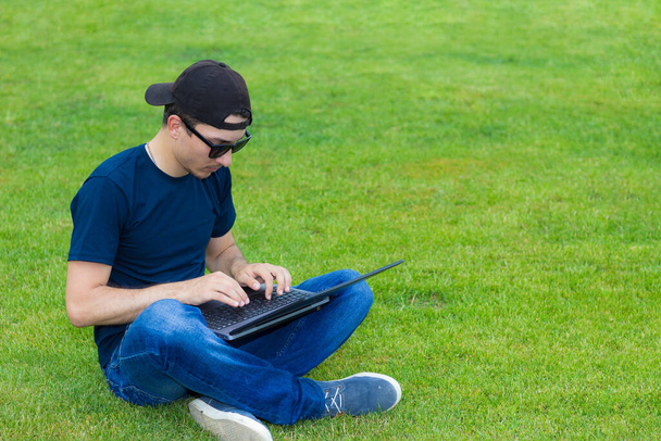 Фрилансер с ноутбуком работает на открытом воздухе на зеленой лужайке
. - Фото, изображение