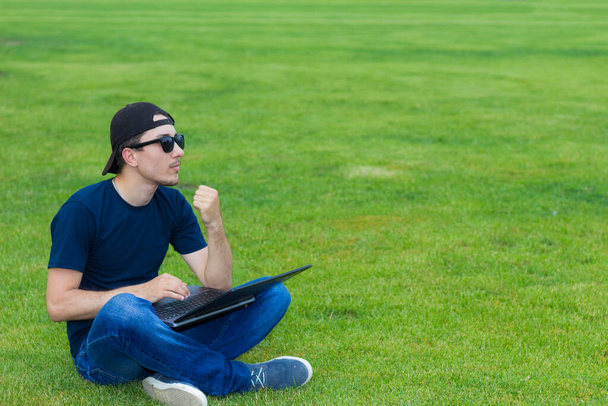 Freelance avec un ordinateur portable fonctionne en plein air sur une pelouse verte
. - Photo, image
