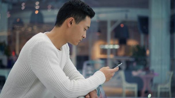 Side view of hamdsome asian man scrolling phone on big mall background - 写真・画像