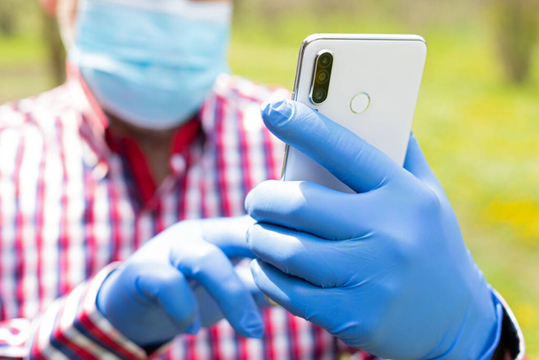 Ederly man's hands wearing surgical mask and gloves talking on the phone outdoors - Foto, Bild