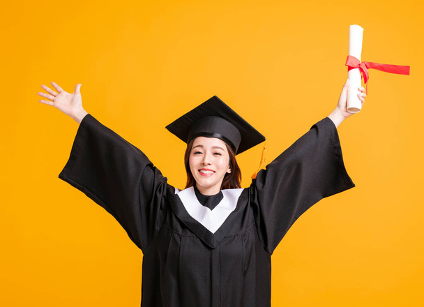 jovem feliz em vestidos de graduação segurando diploma com gesto de sucesso
 - Foto, Imagem