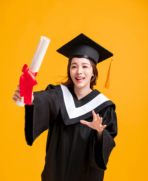 szczęśliwa młoda kobieta w sukniach dyplomowych i pokazując dyplom  - Zdjęcie, obraz