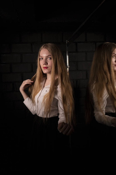 Blonde by the mirror in a white shirt in a dark room. - Foto, afbeelding