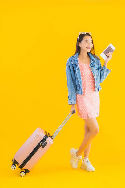 Портрет красива молода азіатка з багажною сумкою з паспортом і квитком на посадковий талон на жовтому ізольованому тлі
 - Фото, зображення