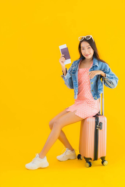 Portrait beautiful young asian woman with luggage travel bag with passport and boarding pass ticket on yellow isolated background - 写真・画像