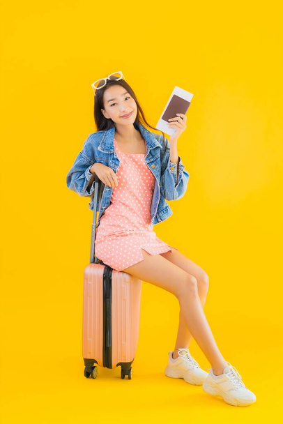 Portrait beautiful young asian woman with luggage travel bag with passport and boarding pass ticket on yellow isolated background - 写真・画像