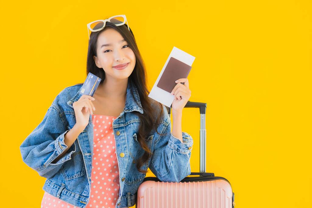 Retrato hermosa joven asiática mujer con equipaje bolsa de viaje con pasaporte y billete de embarque en amarillo aislado fondo
 - Foto, Imagen