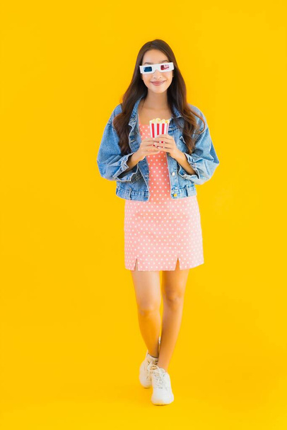 Portret mooie jonge aziatische vrouw genieten gelukkig met telefoon popcorn en bekijk film op geel geïsoleerde achtergrond - Foto, afbeelding