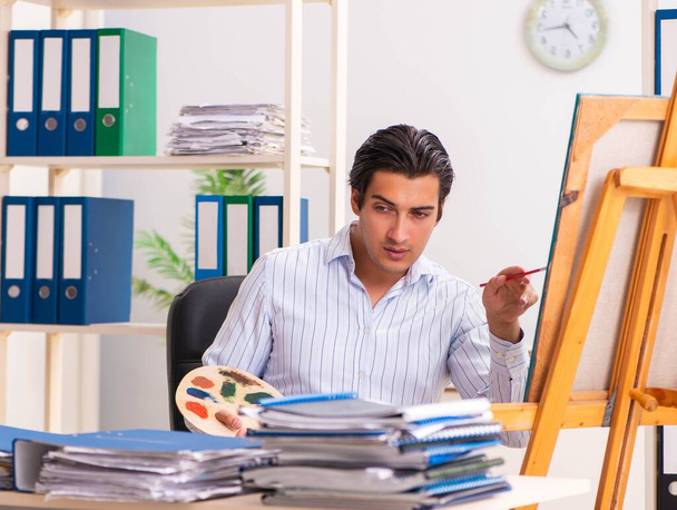 Fiatal jóképű alkalmazott élvezi a festést az irodában - Fotó, kép