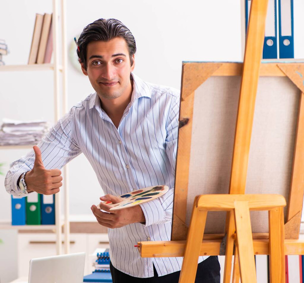 Jonge knappe werknemer geniet van het schilderen op kantoor - Foto, afbeelding