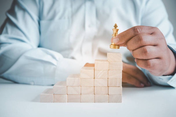 La mano del hombre de negocios recoge ajedrez en un bloque de madera, líder del concepto a la meta
. - Foto, imagen